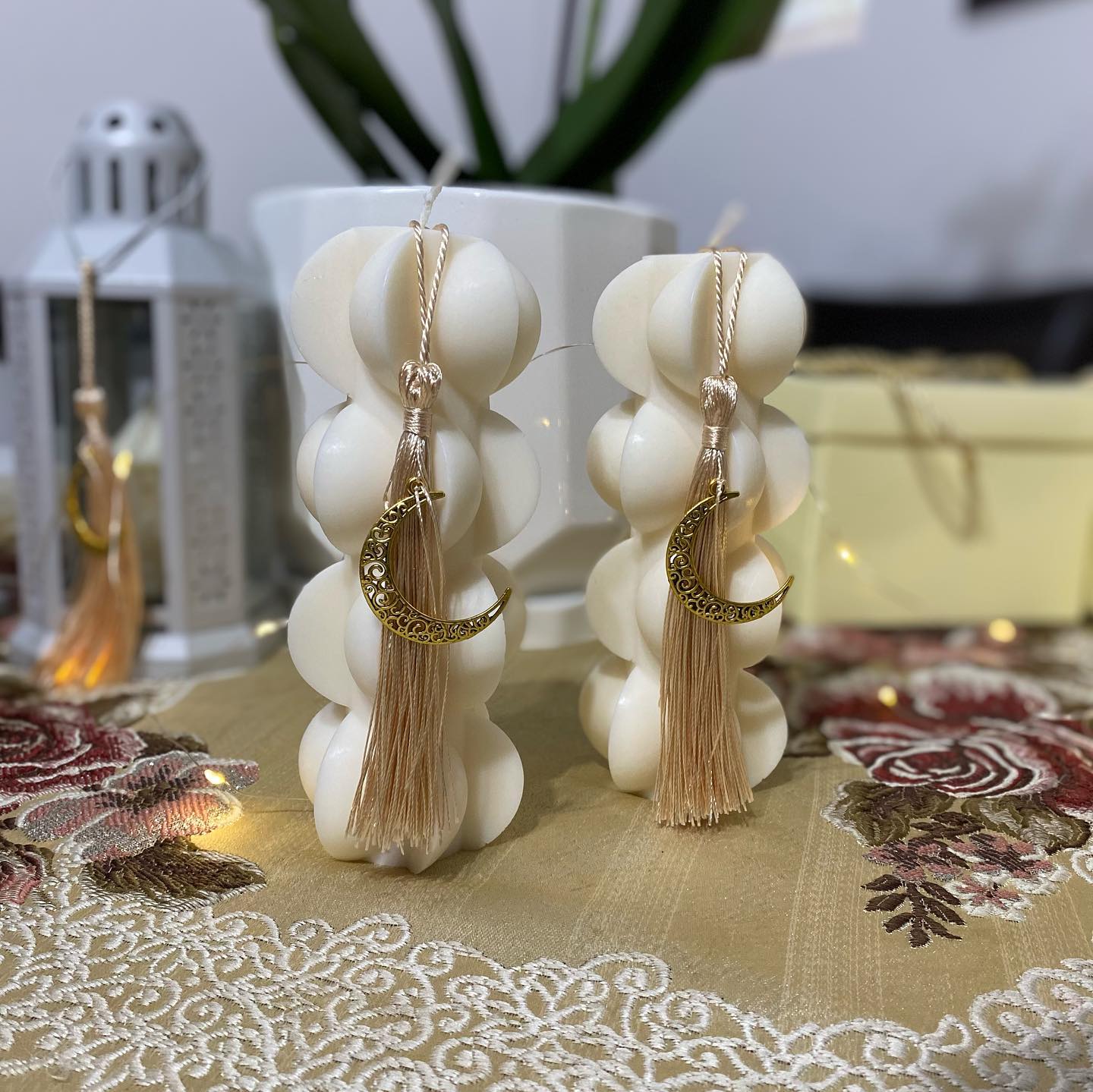 Two white sculptural pillar candles decorated with crescent charms and tassels